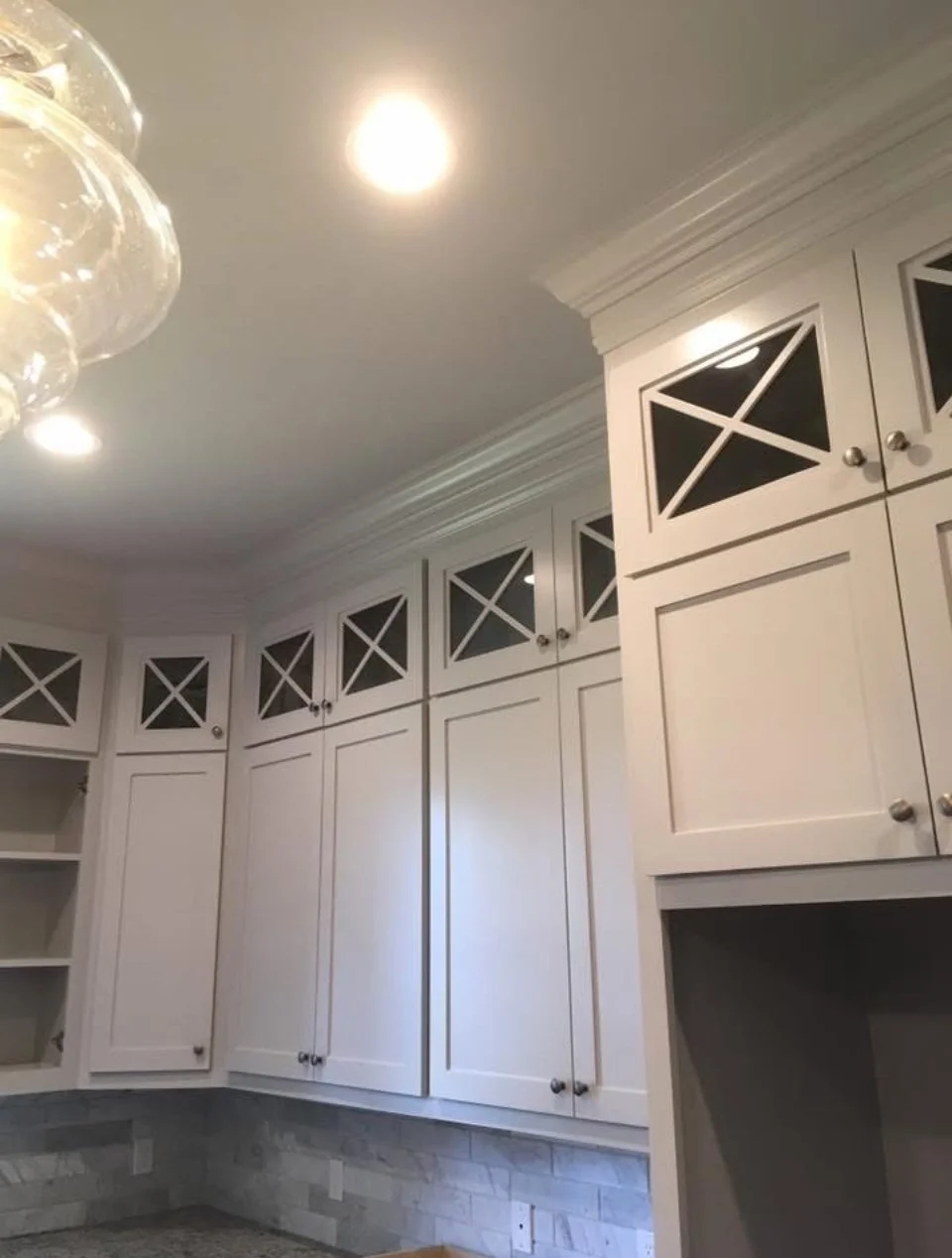 White kitchen cabinets with black glass inserts, crown molding, and a gray brick tile backsplash.
