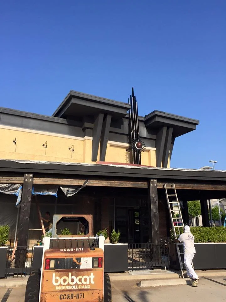 Construction worker standing on a ladder working on the exterior of a building under a blue sky.