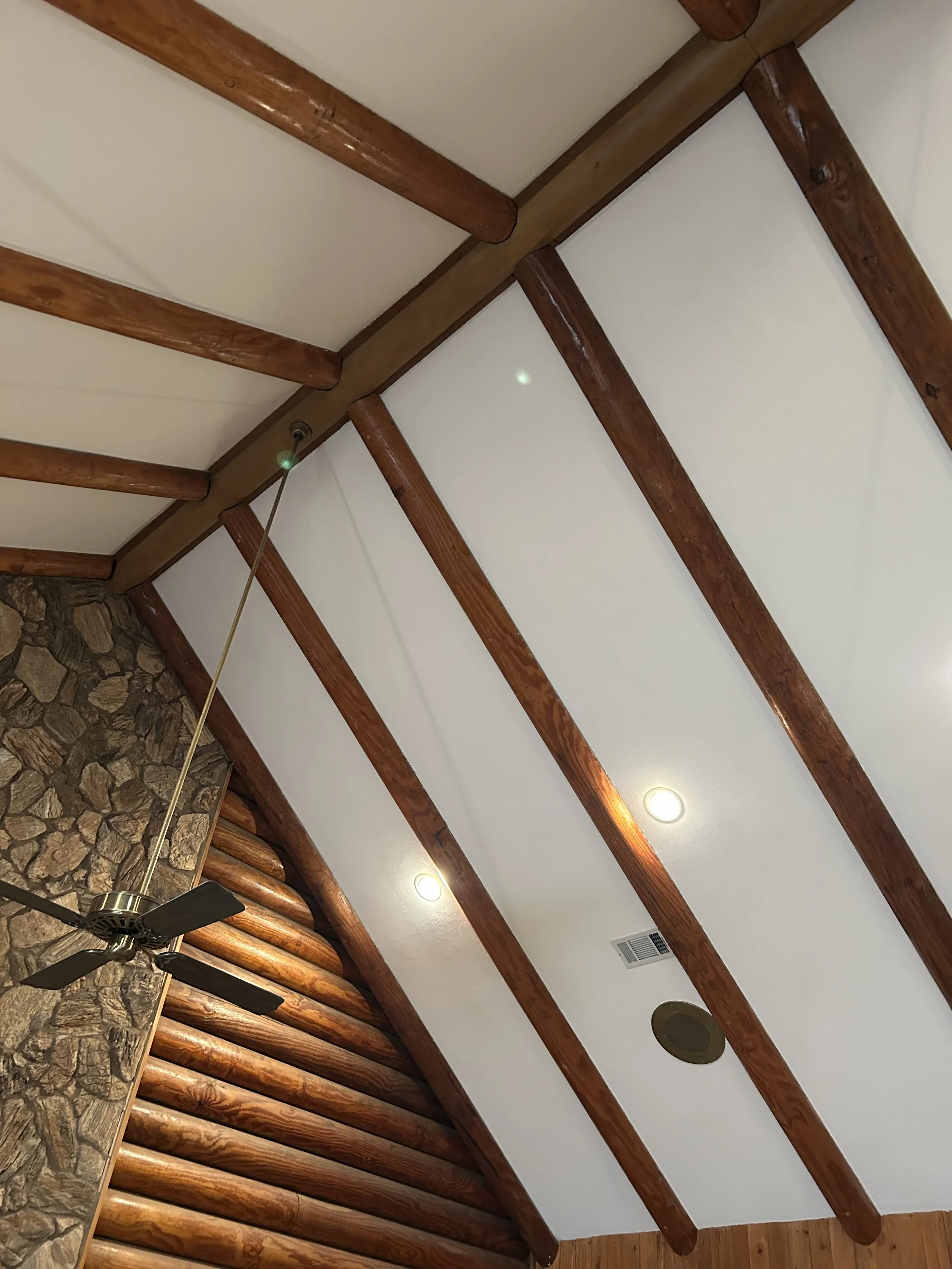 Ceiling of a room with white panels, exposed wooden beams, a ceiling fan, and recessed lighting.