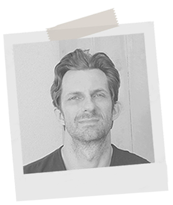 Black and white photo of a man with light hair and beard, looking at the camera.