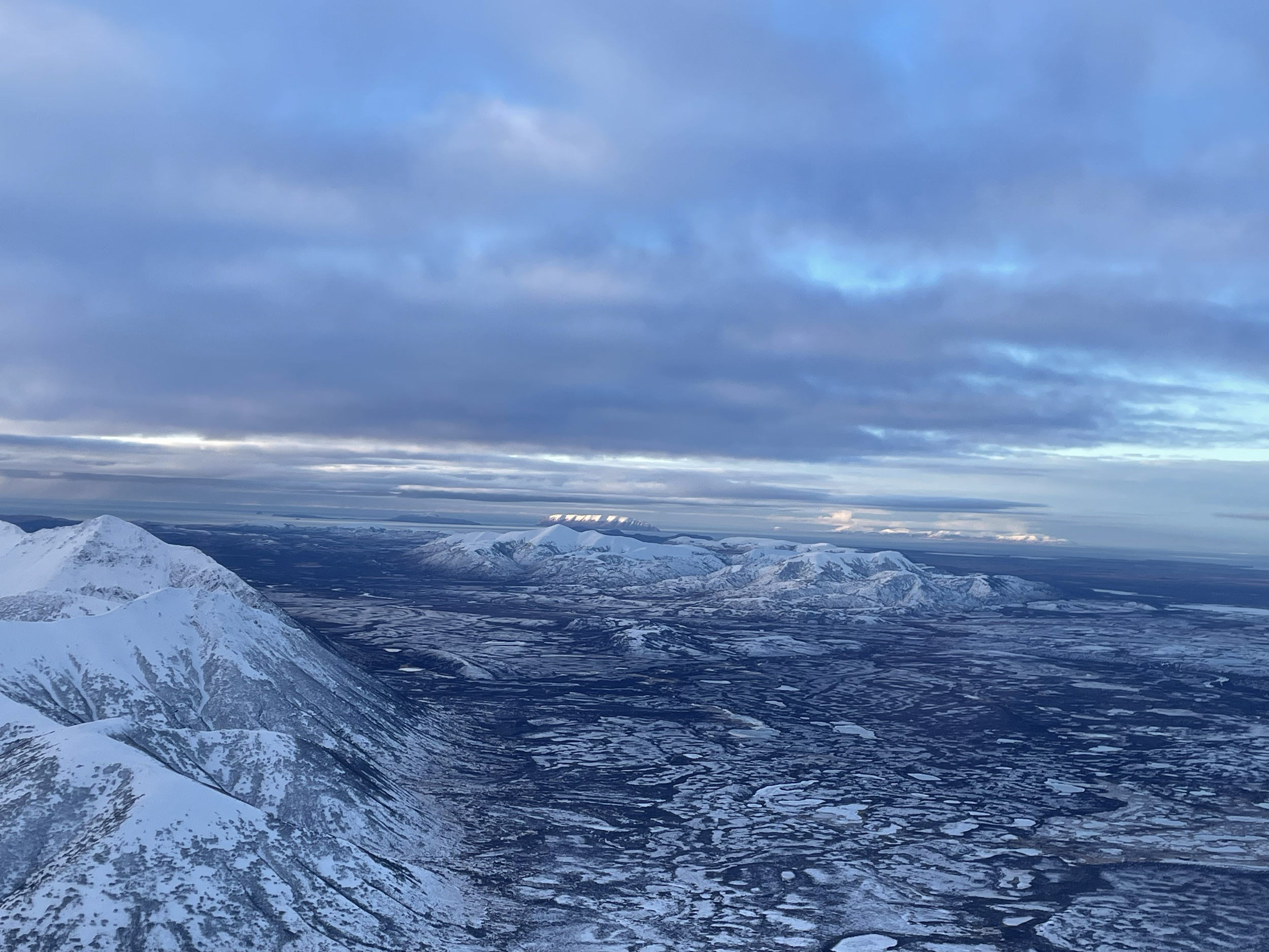 Snow-covered mountains under a cloudy sky with patches of blue in the distance.