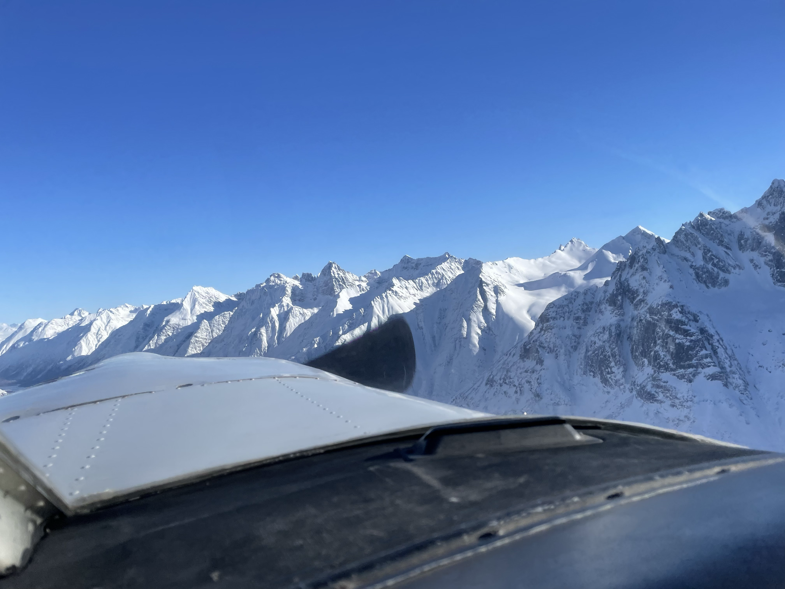 Snow-covered mountain range viewed from an airplane cockpit window.