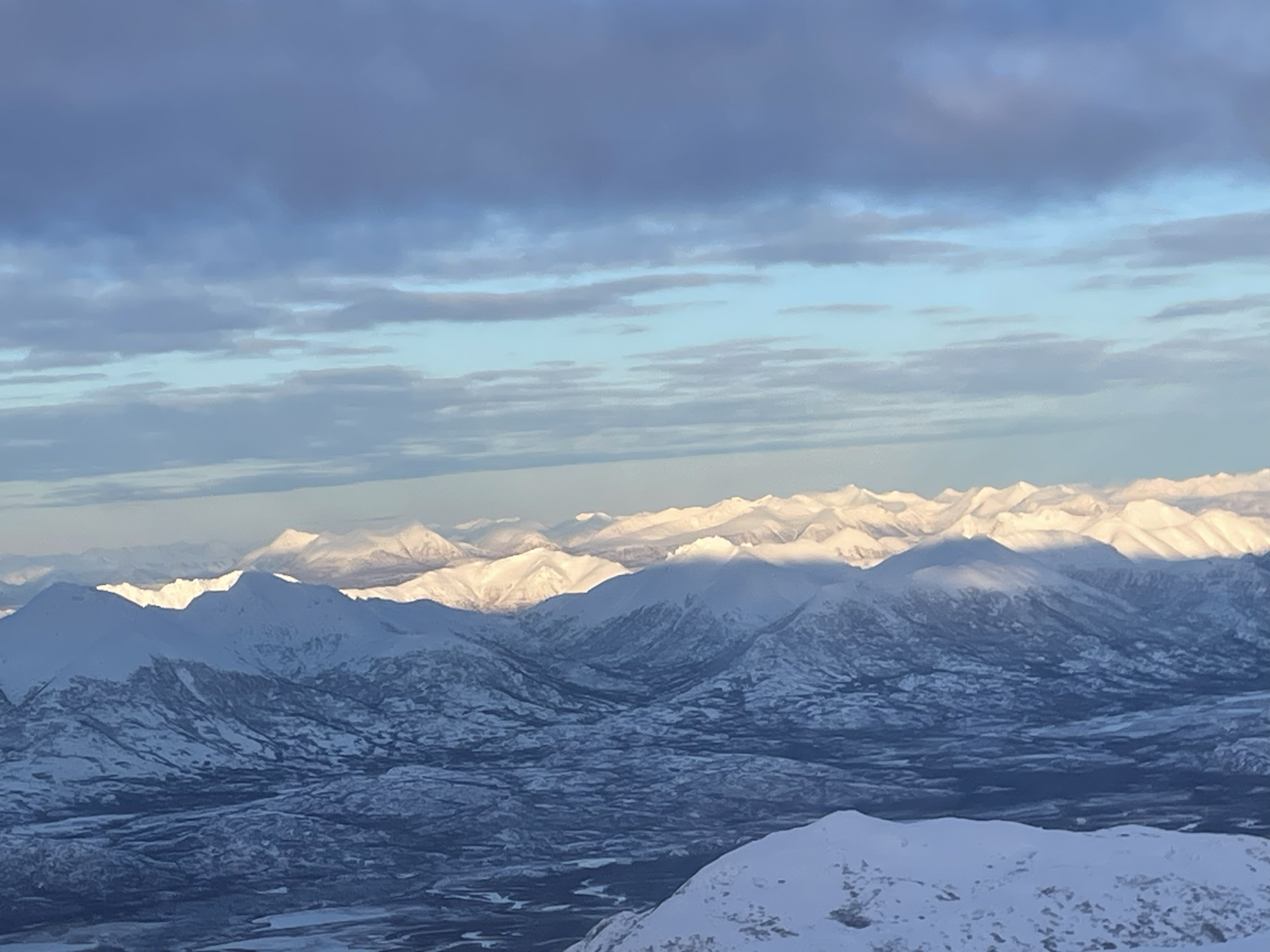 Snow-covered mountain range under a partly cloudy sky.