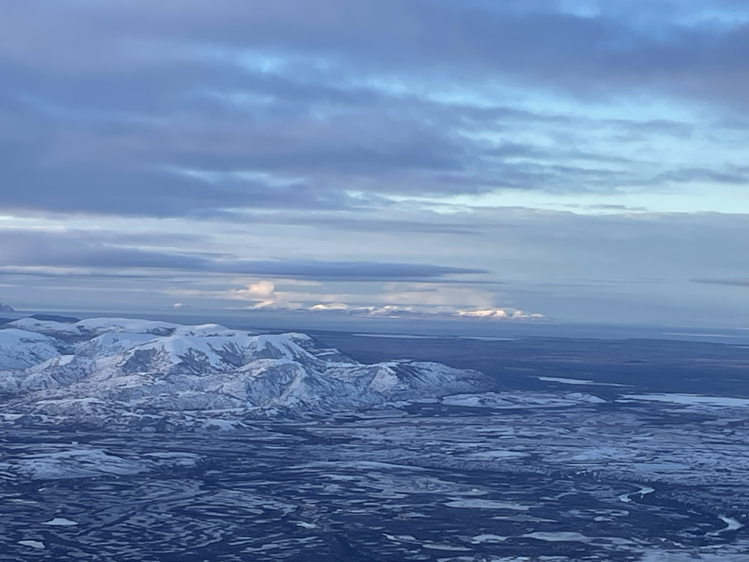Snow-covered mountains under a partly cloudy sky, possibly taken from an aerial perspective.