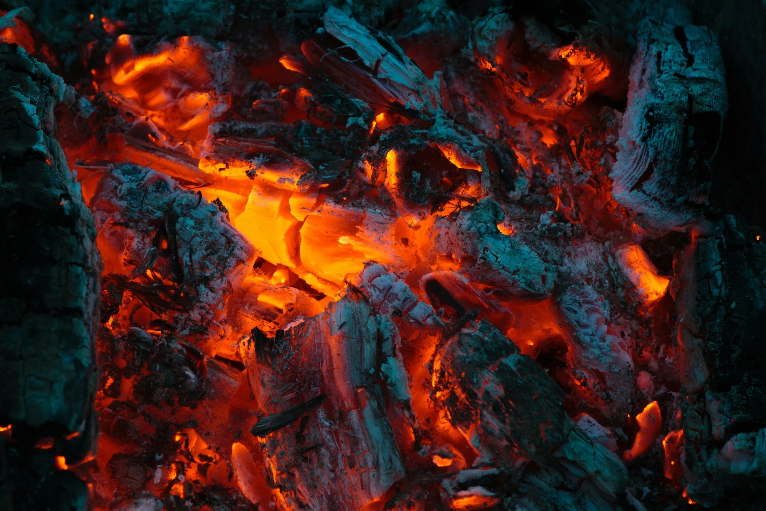 Close-up of glowing red and orange hot embers and ashes from a campfire or fireplace.