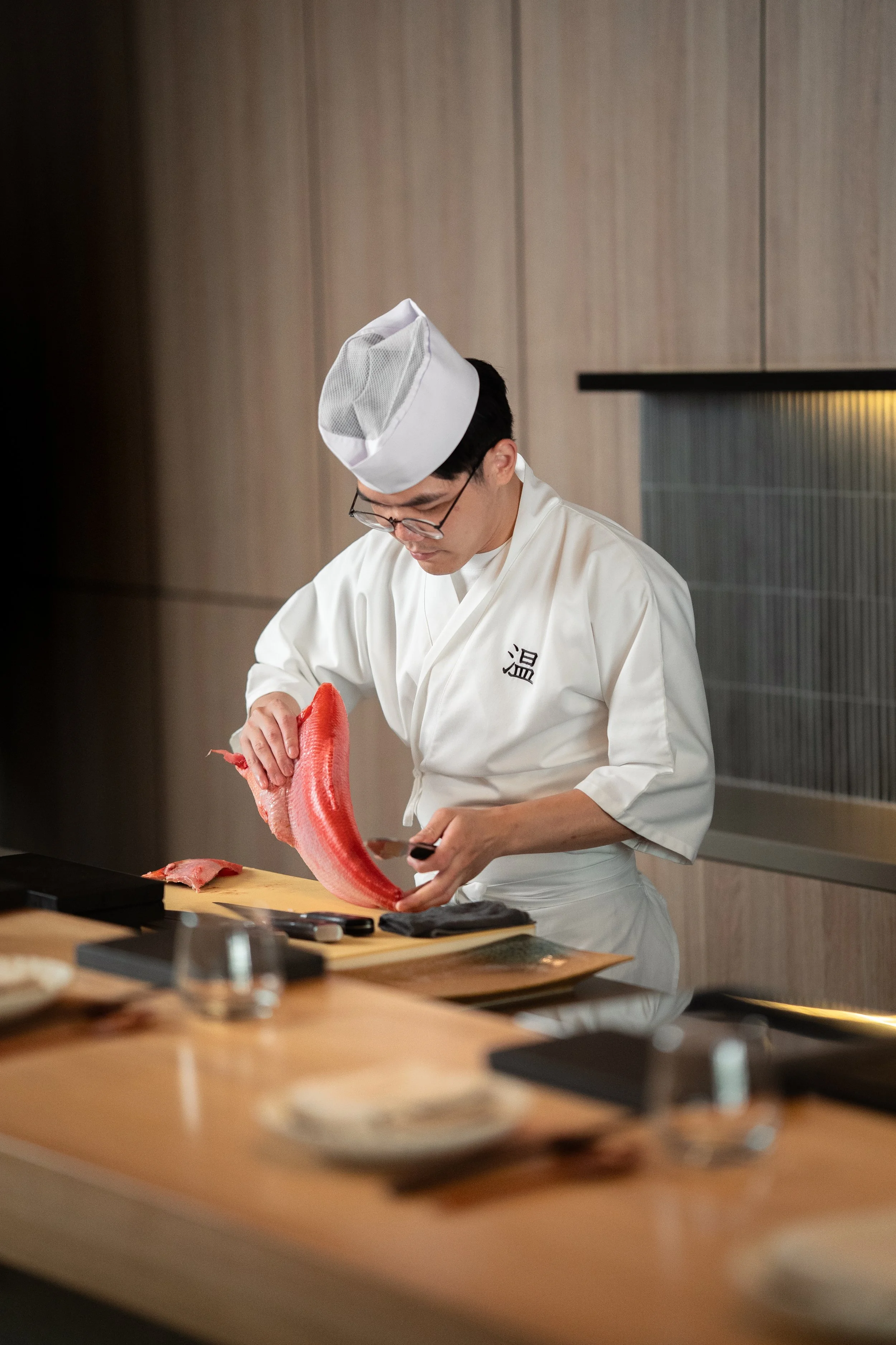 Sushi chef preparing a large piece of fish in a modern sushi restaurant.