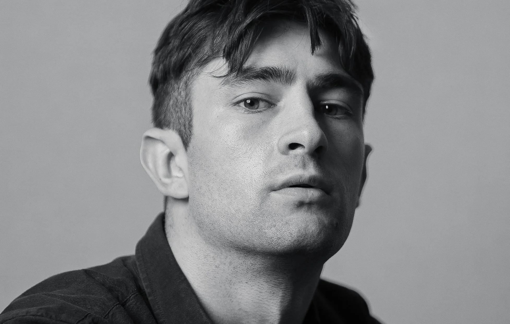 Black and white close-up photograph of a young man with short dark hair, looking slightly to the side with a serious expression, against a plain background.