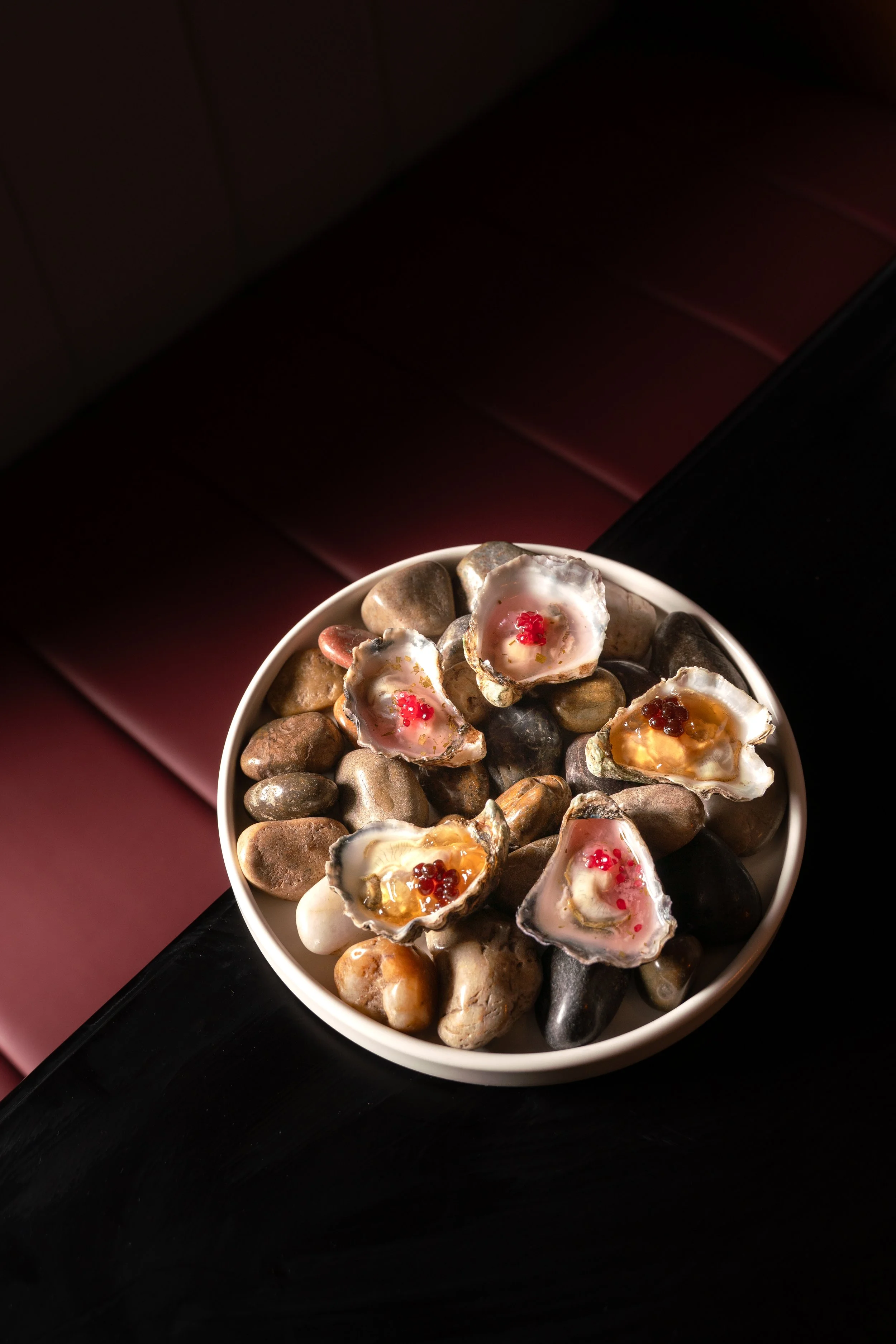 A white bowl filled with rocks and shells containing oysters topped with garnishes at a fancy Melbourne restaurant