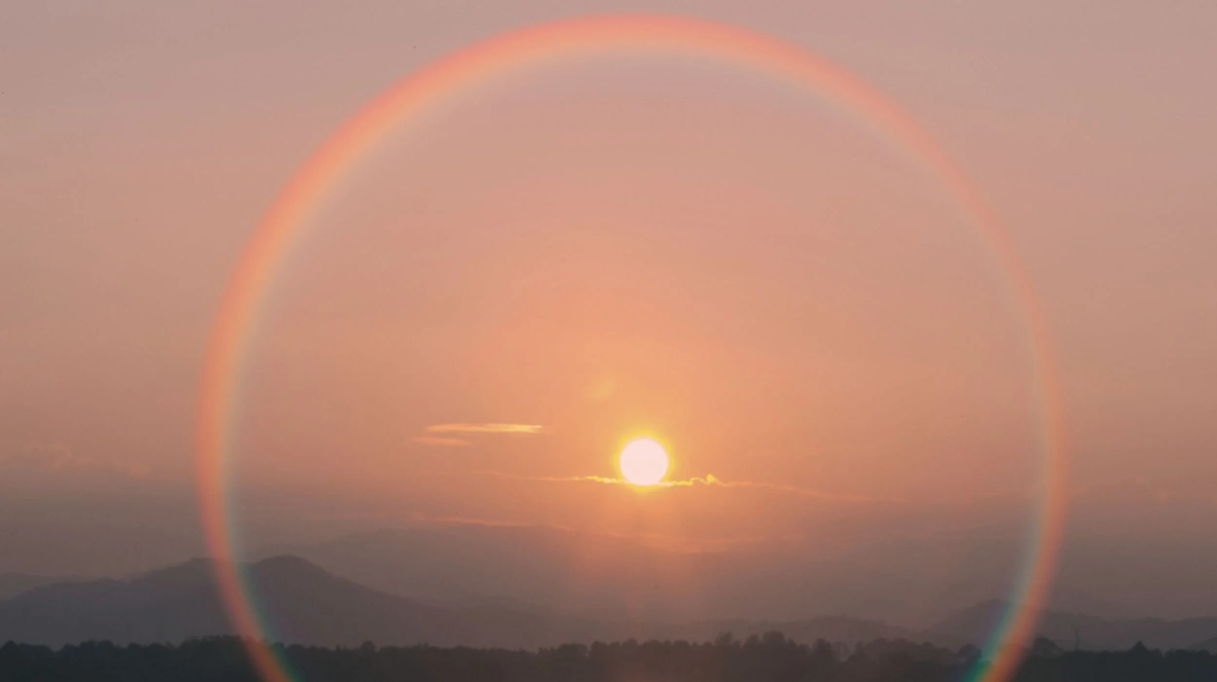 Sunset over soft mountain peaks with a radiant rainbow halo surrounding the sun, symbolizing hope, renewal, and the integrative nature of healing through Embodied Soul Psychotherapy™.
