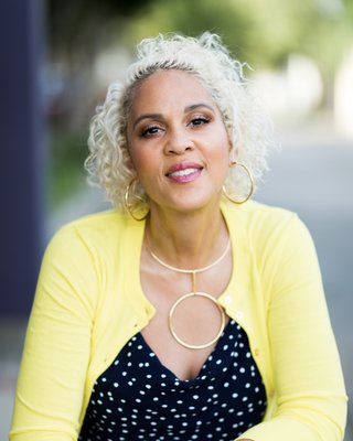 Dr. Chanin Hardwick, founder of Embodied Soul Psychotherapy™, sitting outdoors in a yellow cardigan and hoop earrings, radiating warmth, grounded presence, and compassionate expertise in trauma-informed care.