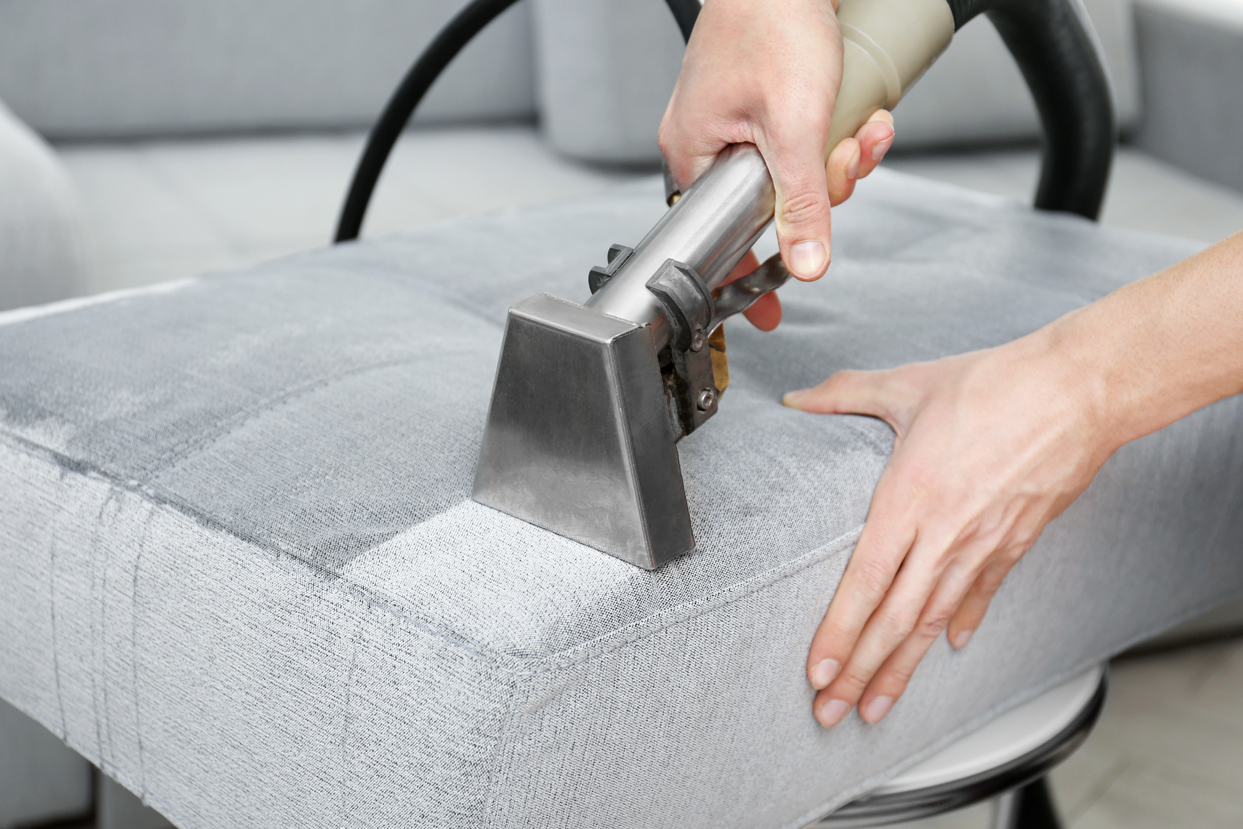 Person steaming a gray upholstered piece of furniture with a handheld steamer.