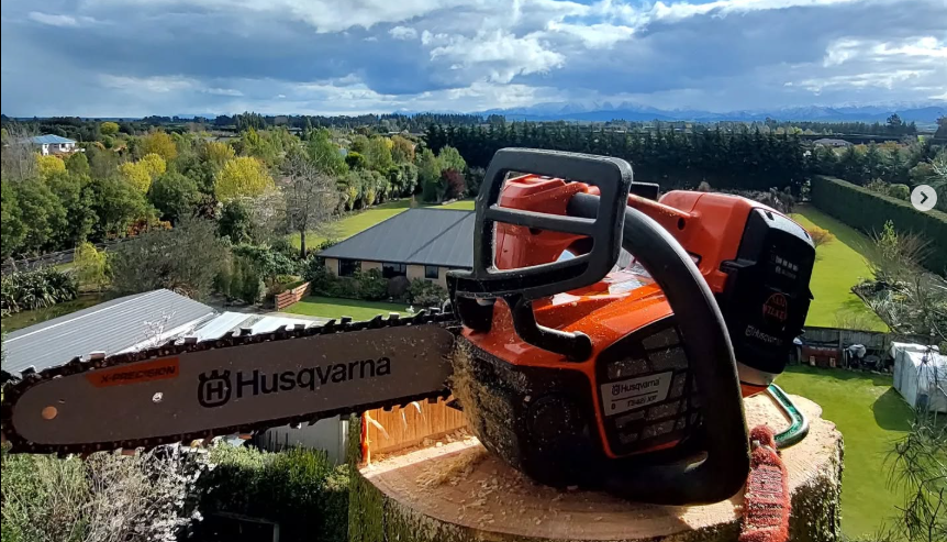 Large orange chainsaw with Husqvarna branding resting on a tree stump, overlooking the Canterbury landscape after a succesful project.