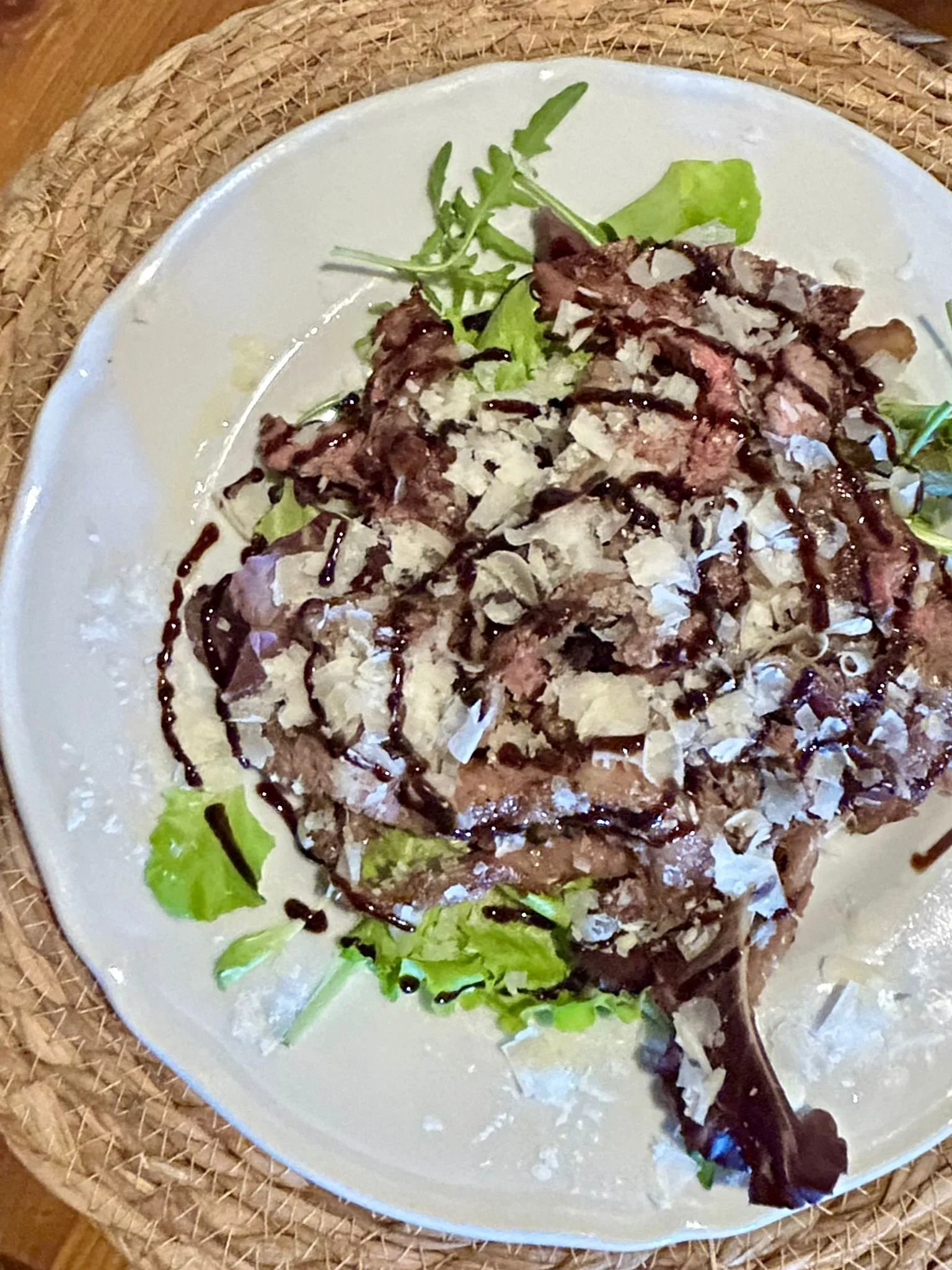 Insalata con rucola, scaglie di formaggio, carne, accompagnata da una salsa balsamica.
