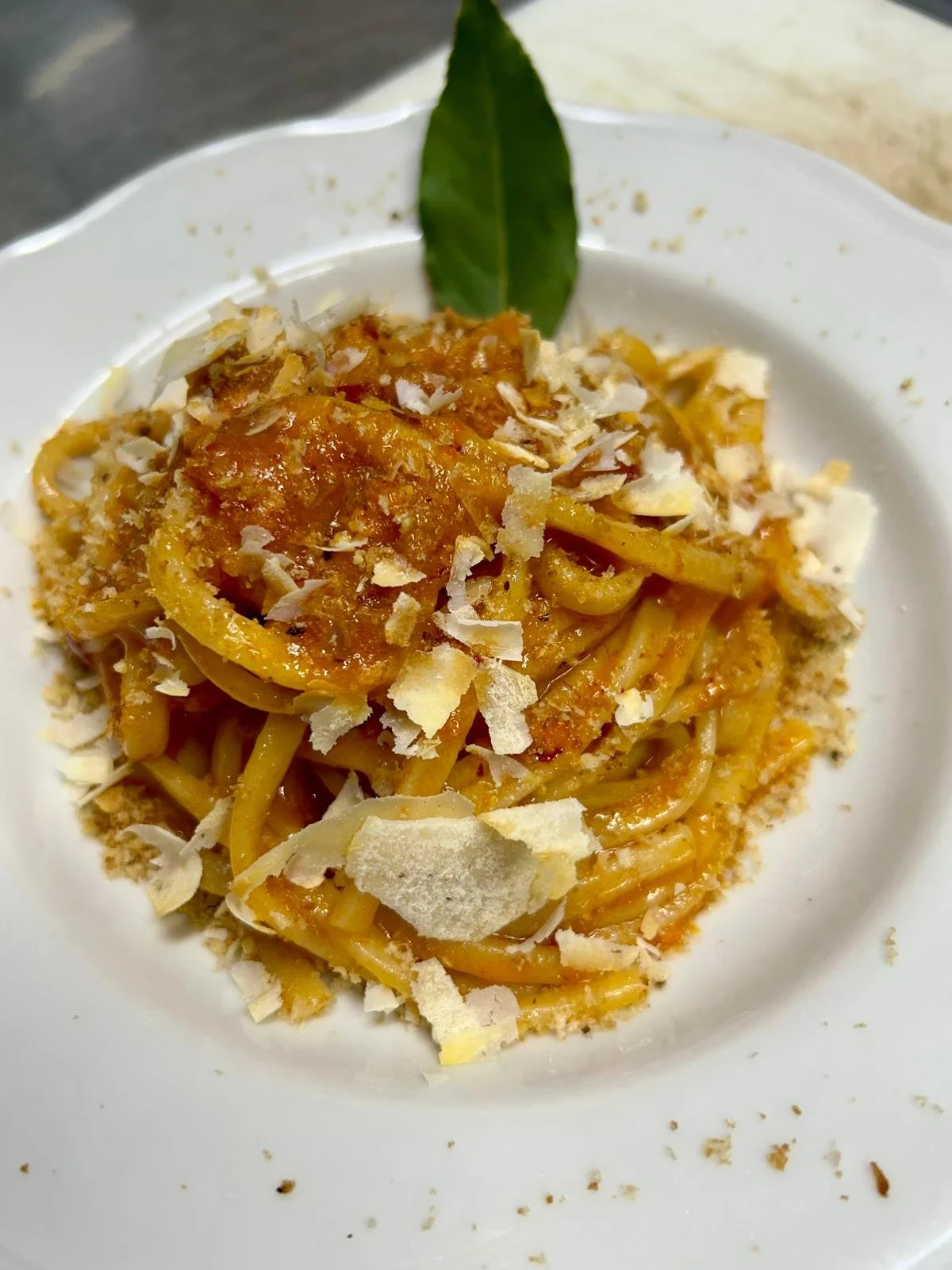 Piattino di spaghetti con salsa di pomodoro, scaglie di formaggio e una foglia di alloro decorativa.