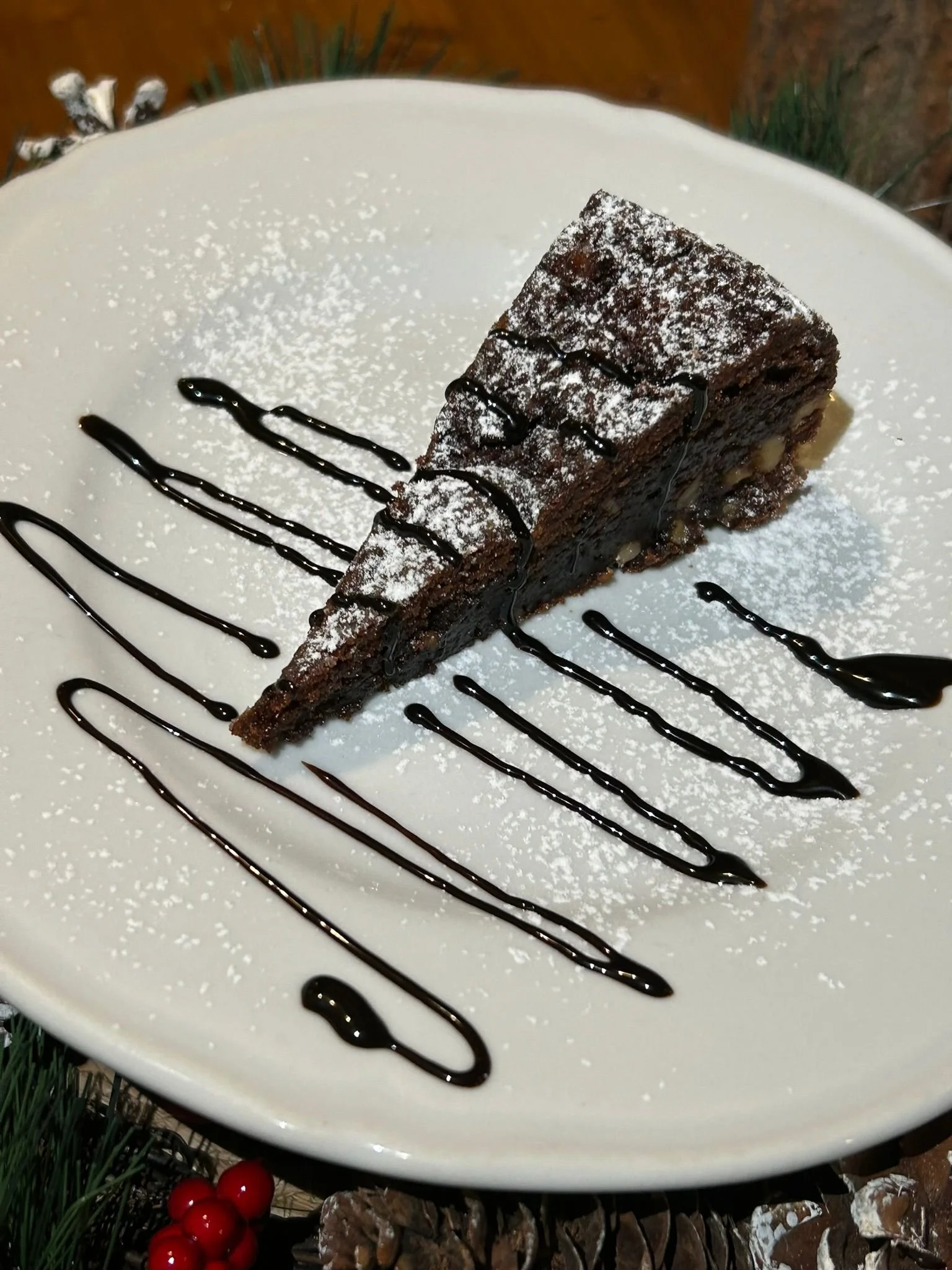 Una fetta di torta al cioccolato decorata con cioccolato fondente a fili e zucchero a velo su un piatto bianco.