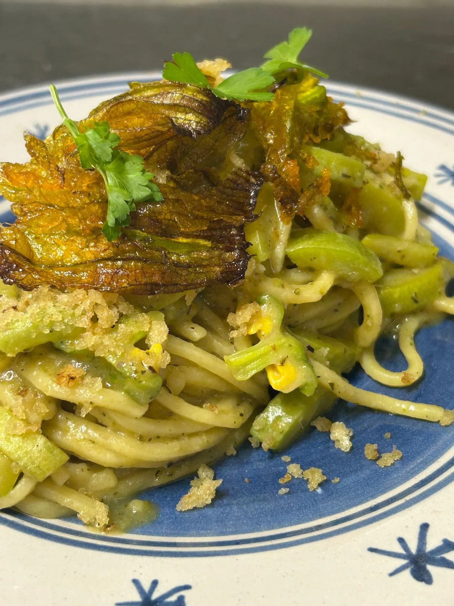 Piatto di pasta con crema e verdure, con guarnitura di foglie di erbe aromatiche e crostini dorati.