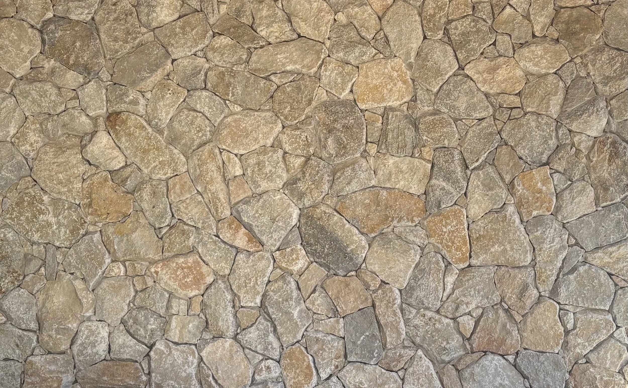 Close-up of a stone wall with irregularly shaped, tan, brown, and gray stones fitted together.