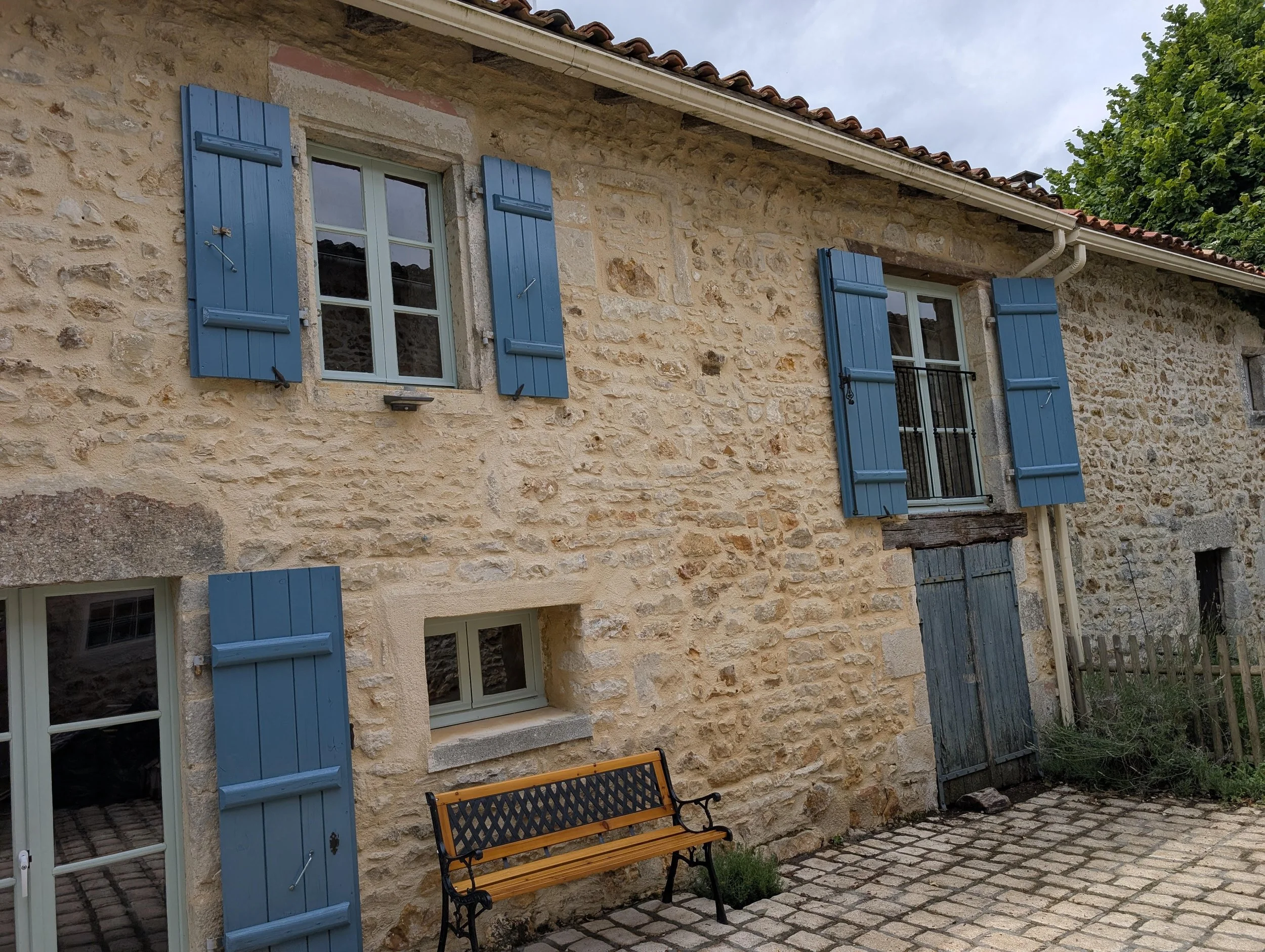 Stone house with blue window shutters, a black iron bench, and cobblestone patio.
