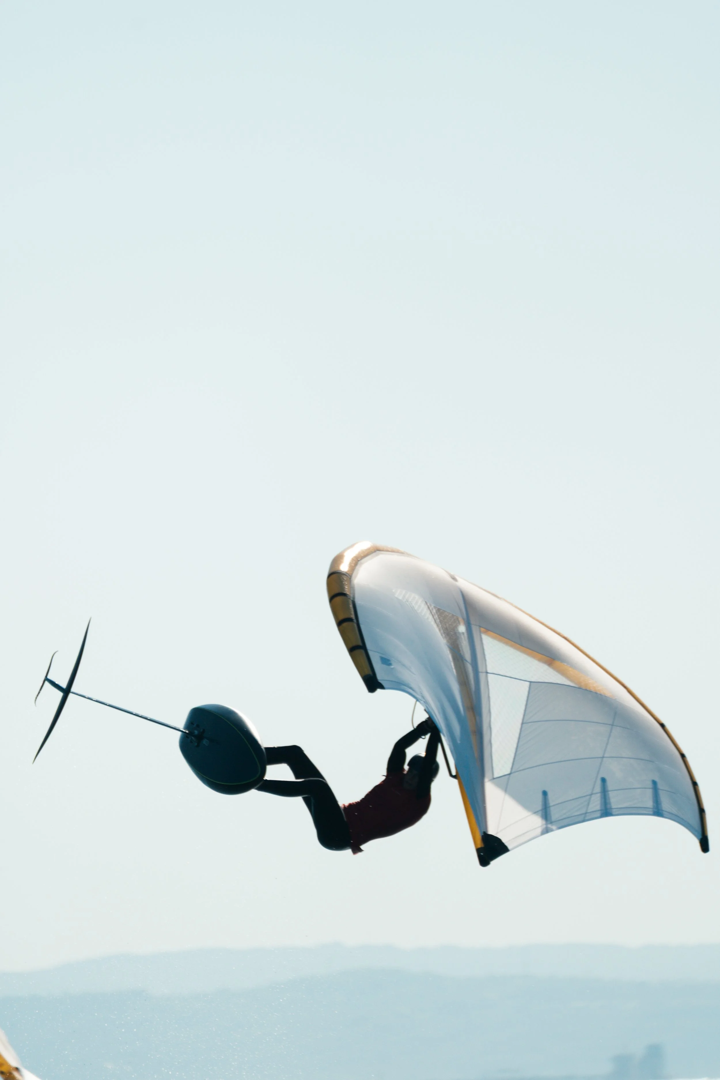 A person wearing a red shirt appears to be hang gliding or paragliding, with the sky and distant landscape below.