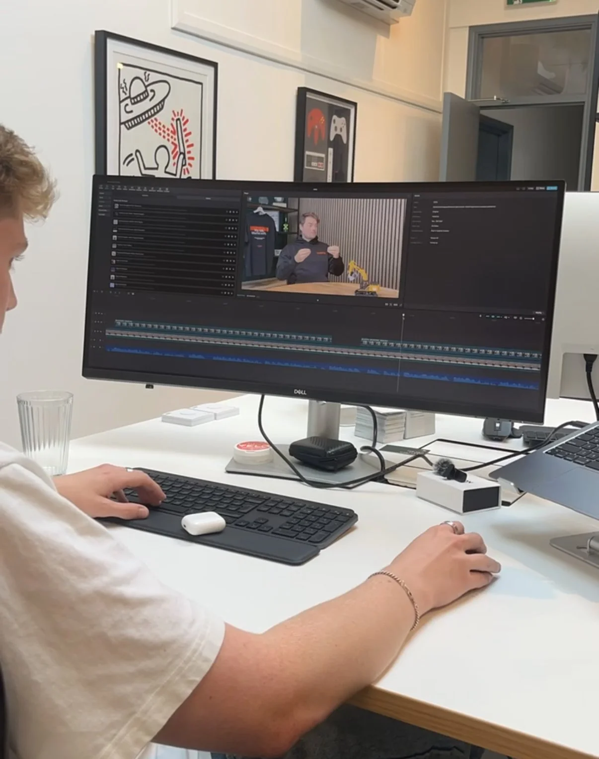 Person editing a video on a computer monitor in an office, with artwork on the wall in the background.