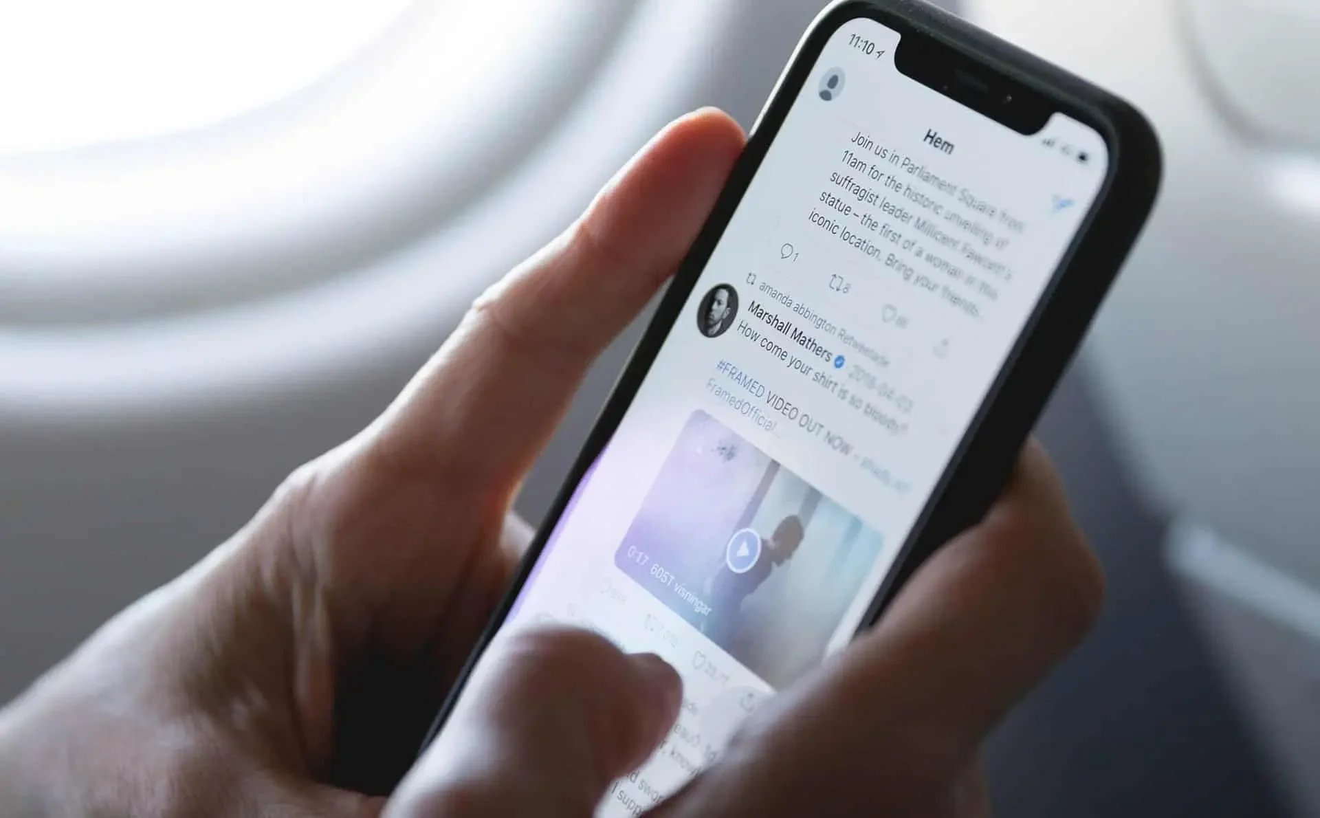 A person holding a smartphone with a social media app open, showing a post about a protest or event, with a video thumbnail and text.