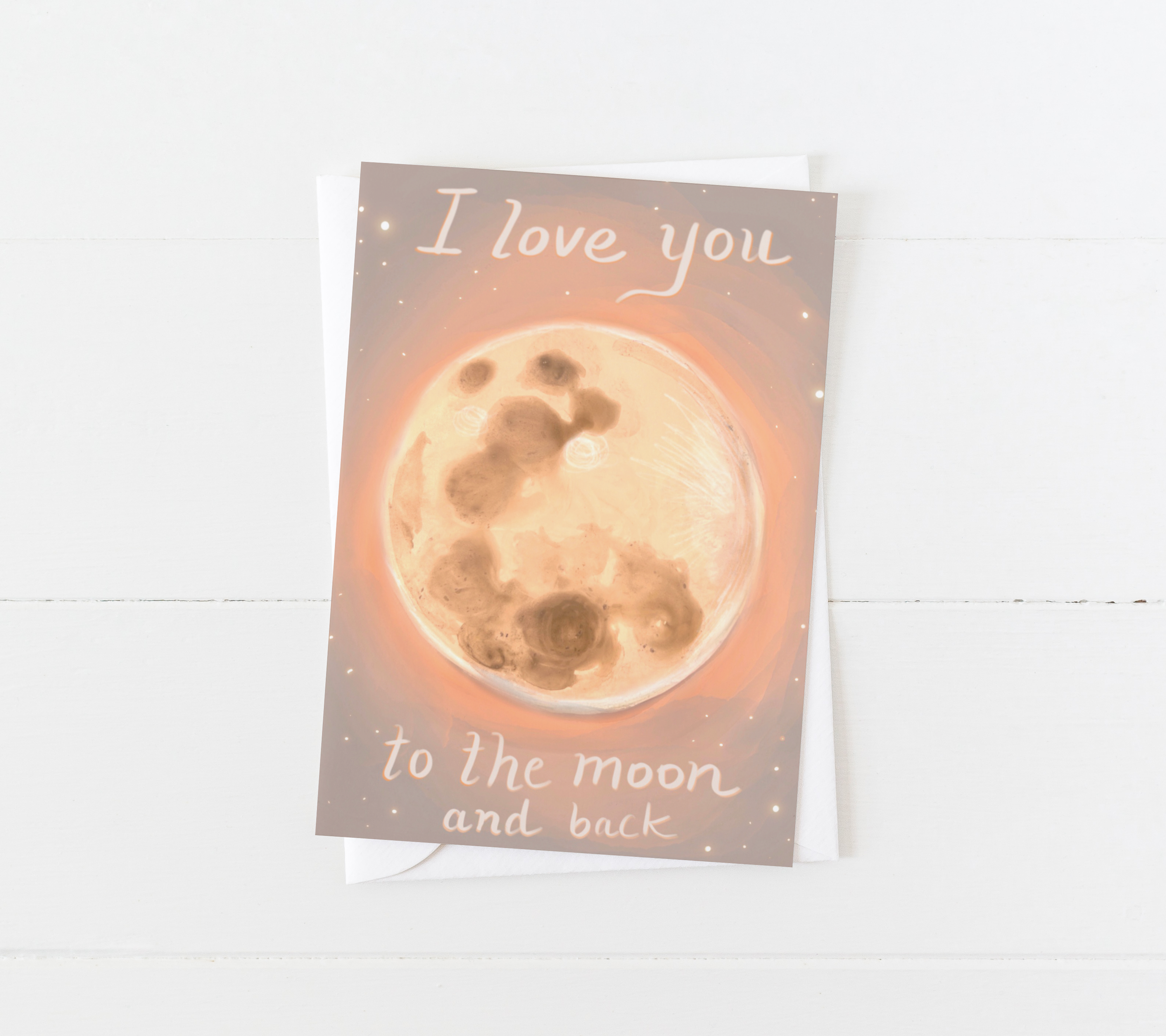Hand holding a greeting card illustrated with a glowing full moon and the phrase “I love you to the moon and back” – artwork by Briana Corr Scott
