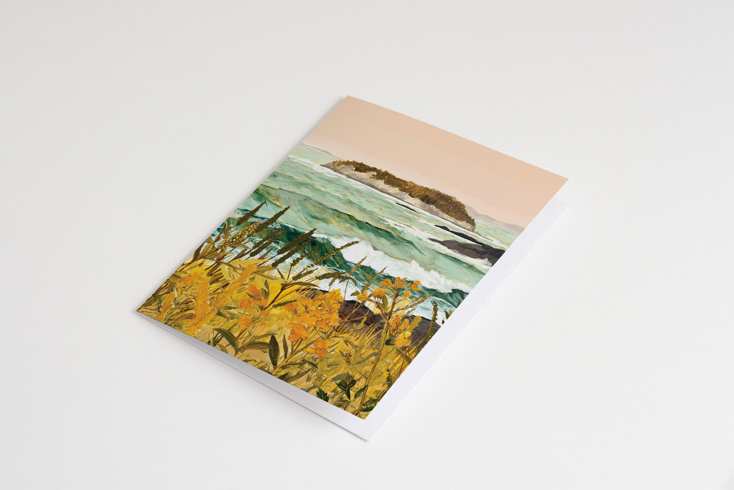 Greeting card featuring a dramatic seascape with waves crashing toward a distant island, golden wildflowers and tall grasses in the foreground, and a peach sky overhead.