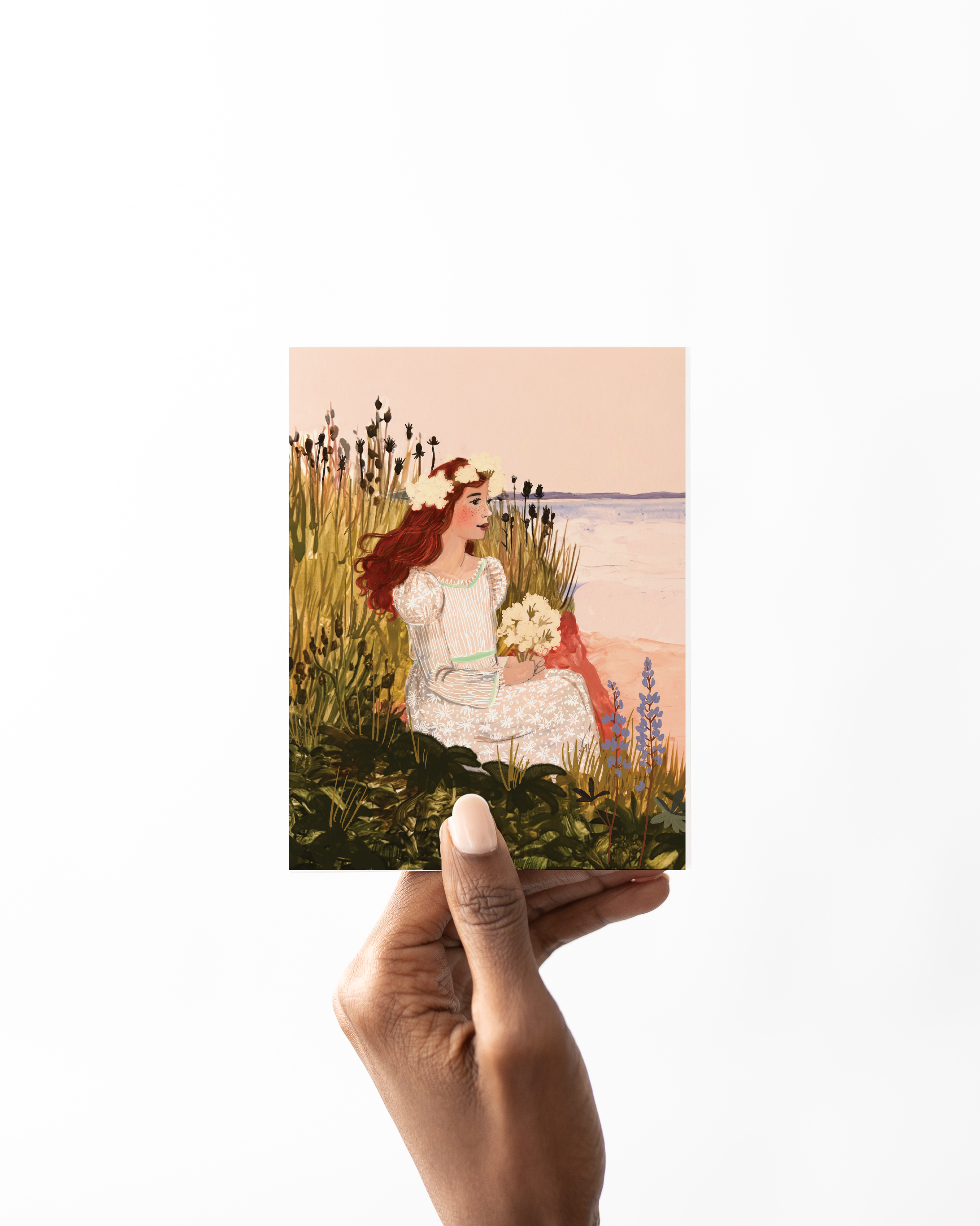 Anne of Green Gables sitting in a coastal meadow holding white flowers, wearing a floral dress and crown, with the sea in the background – artwork by Briana Corr Scott