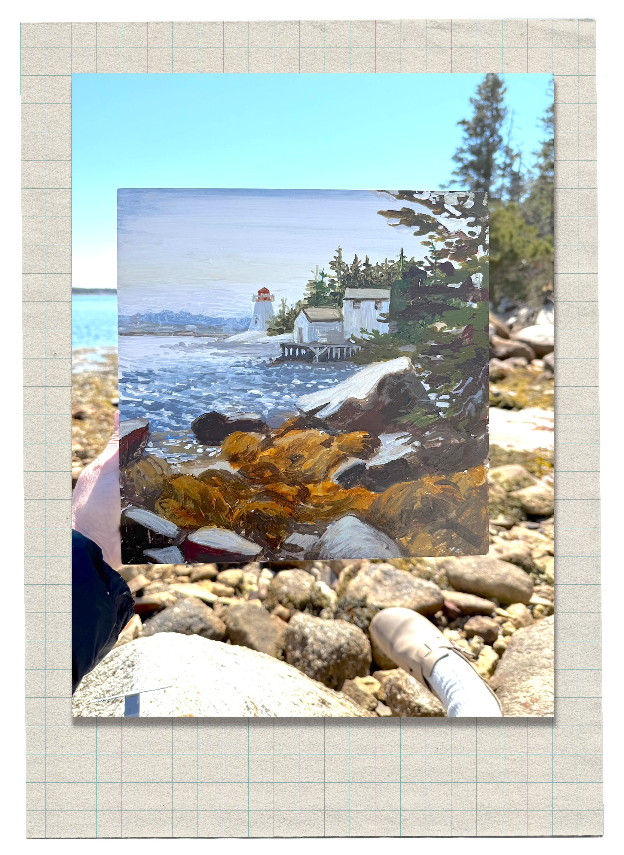 A person holding a painting of a lakeside scene with boats, greenery, and a lighthouse, on a rocky shoreline with trees in the background.