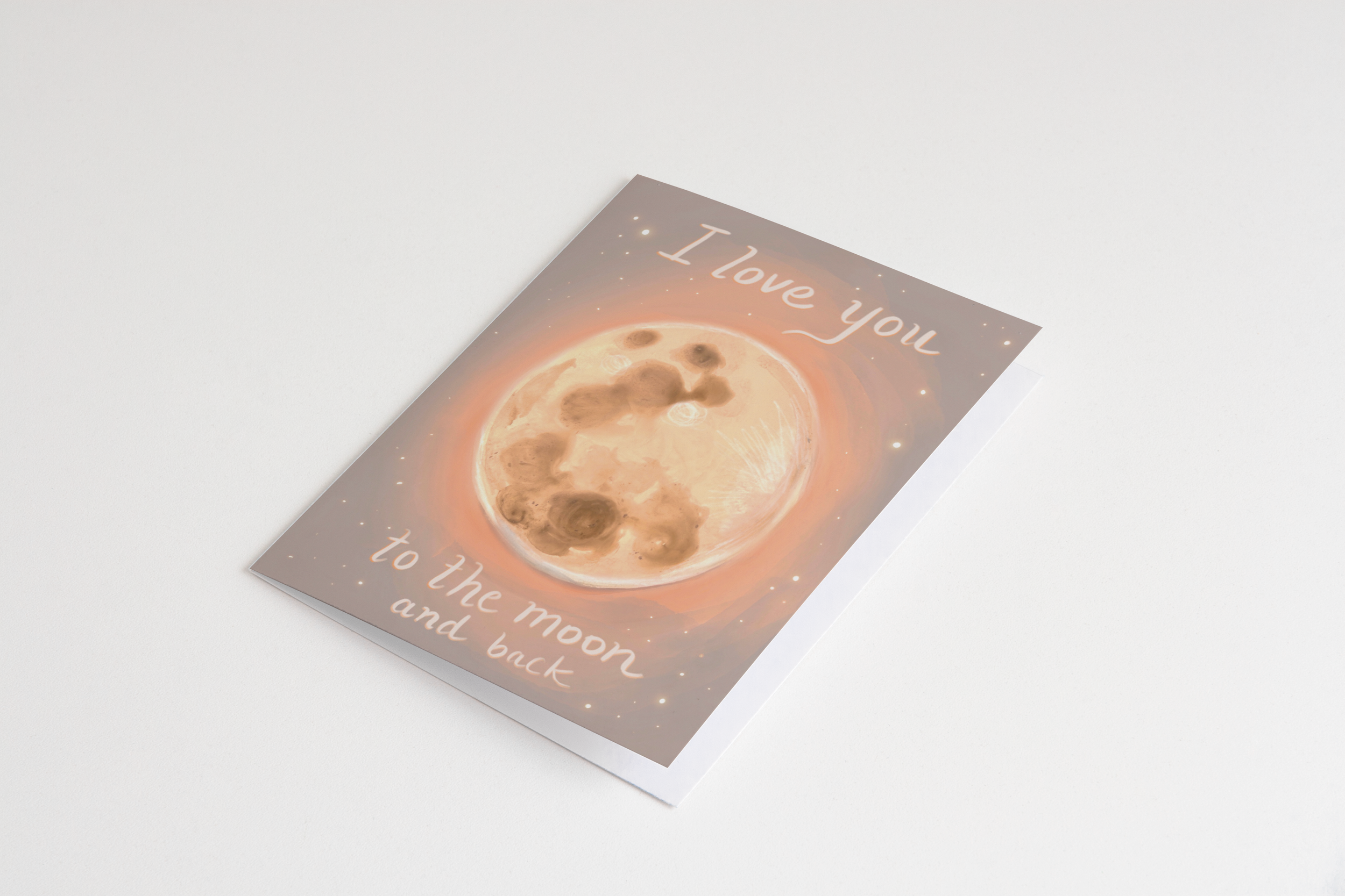 Hand holding a greeting card illustrated with a glowing full moon and the phrase “I love you to the moon and back” – artwork by Briana Corr Scott