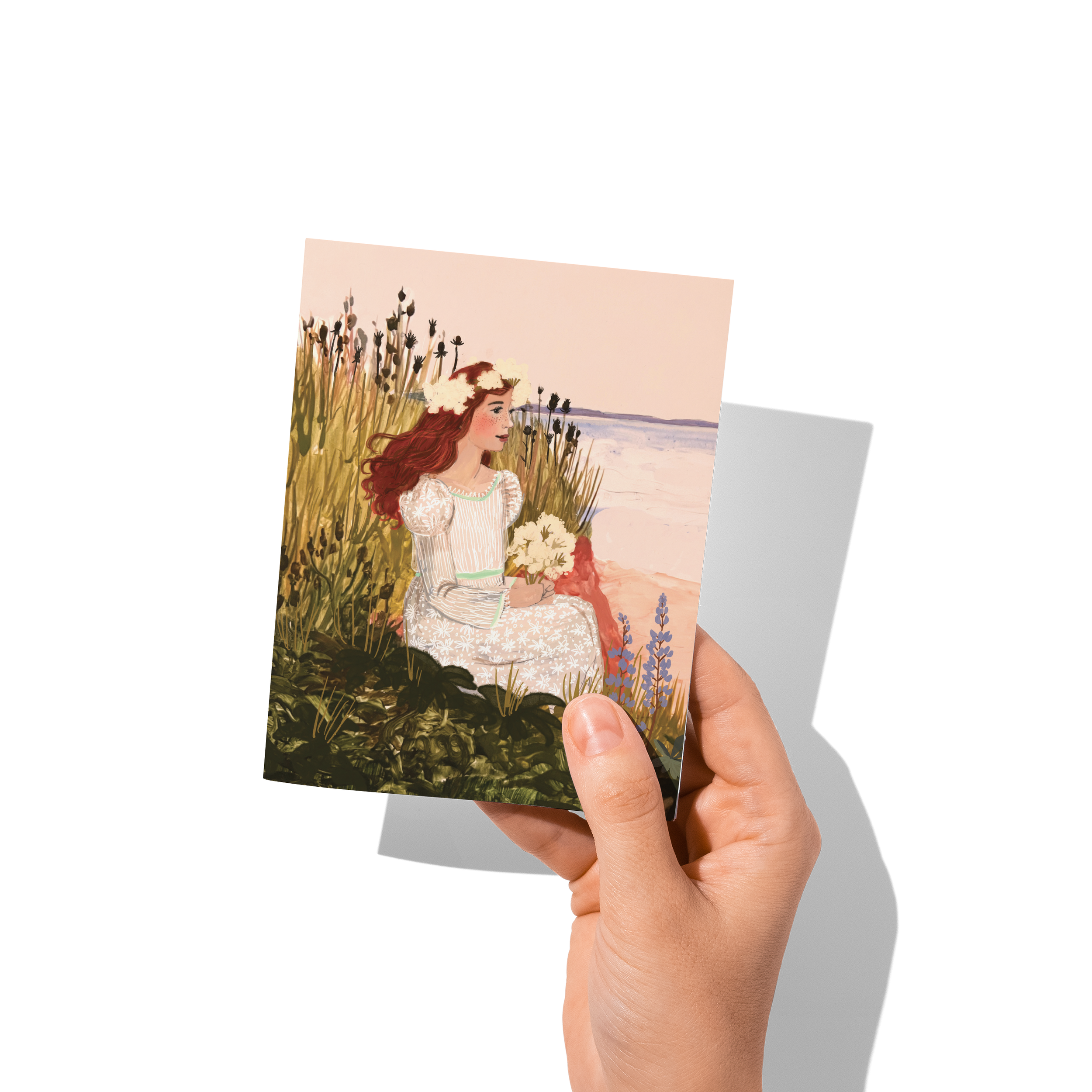Anne of Green Gables sitting in a coastal meadow holding white flowers, wearing a floral dress and crown, with the sea in the background – artwork by Briana Corr Scott
