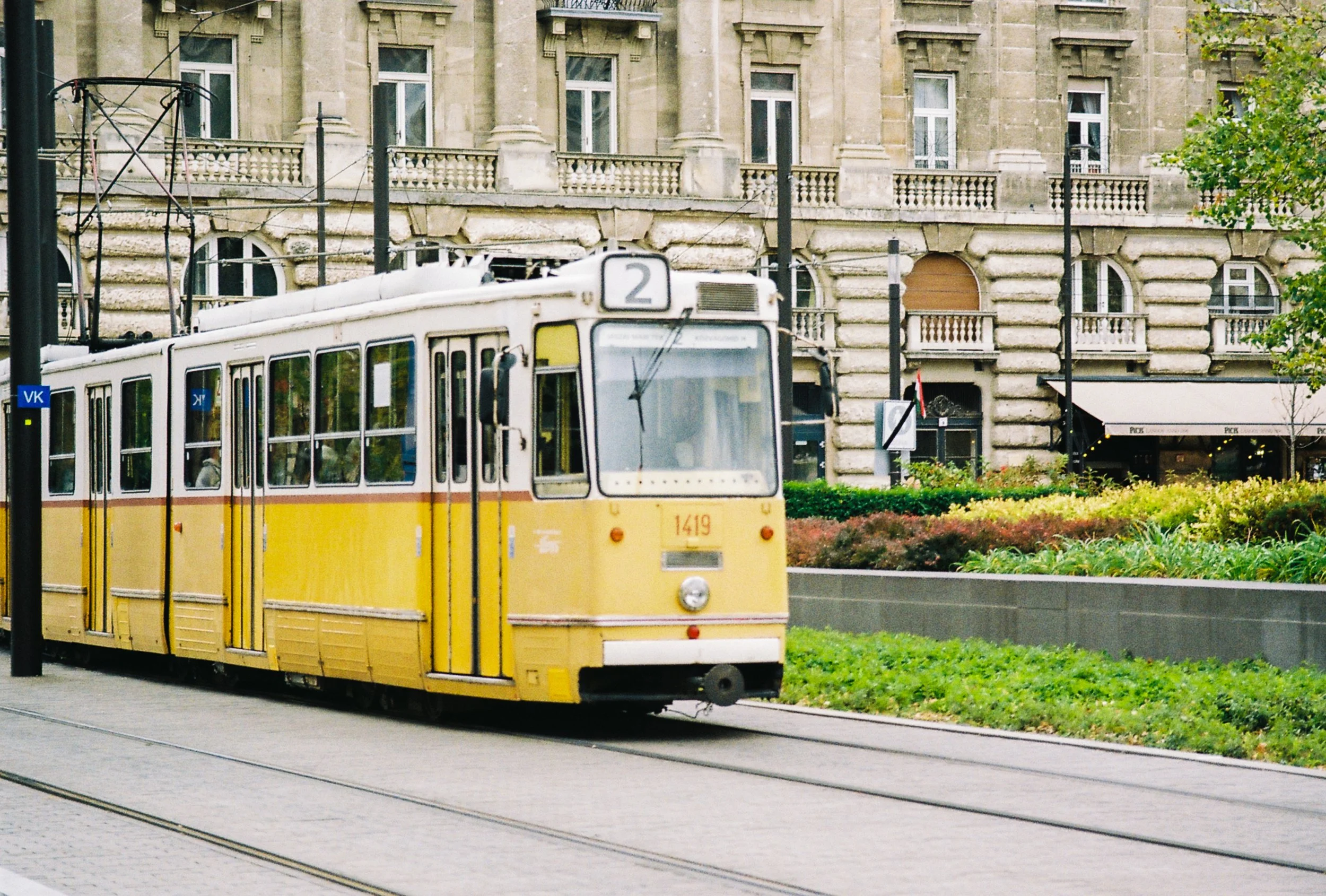 A yellow tram traveling on tracks through an urban area with historic buildings and greenery.
