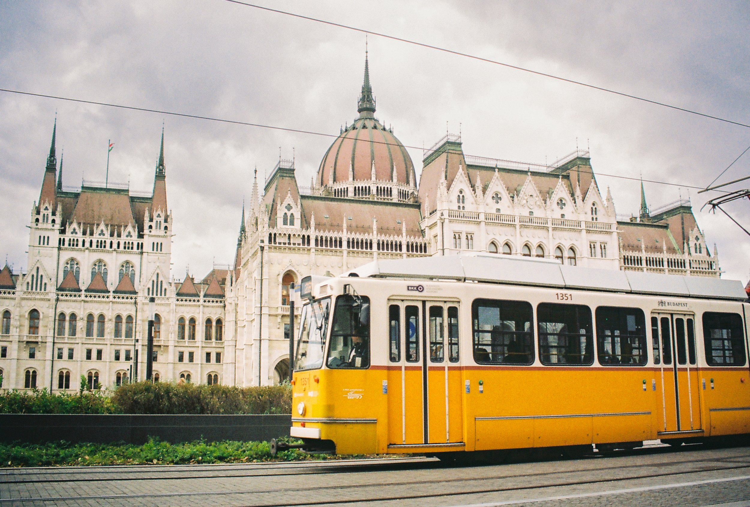 Yellow and white tram in front of a historic building with spires and a large dome in Budapest, Hungary.