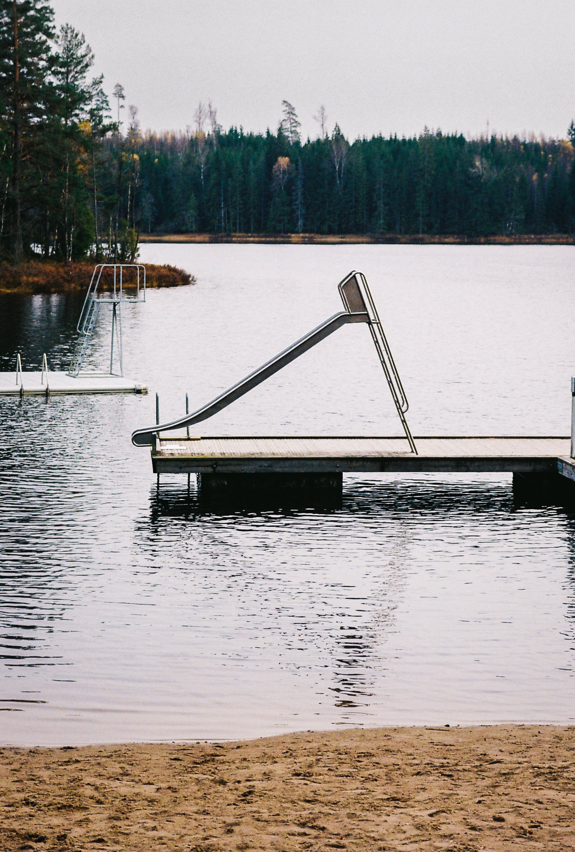 A lakeside dock with metal stairs leading into the water, surrounded by trees and a calm lake, overcast sky.