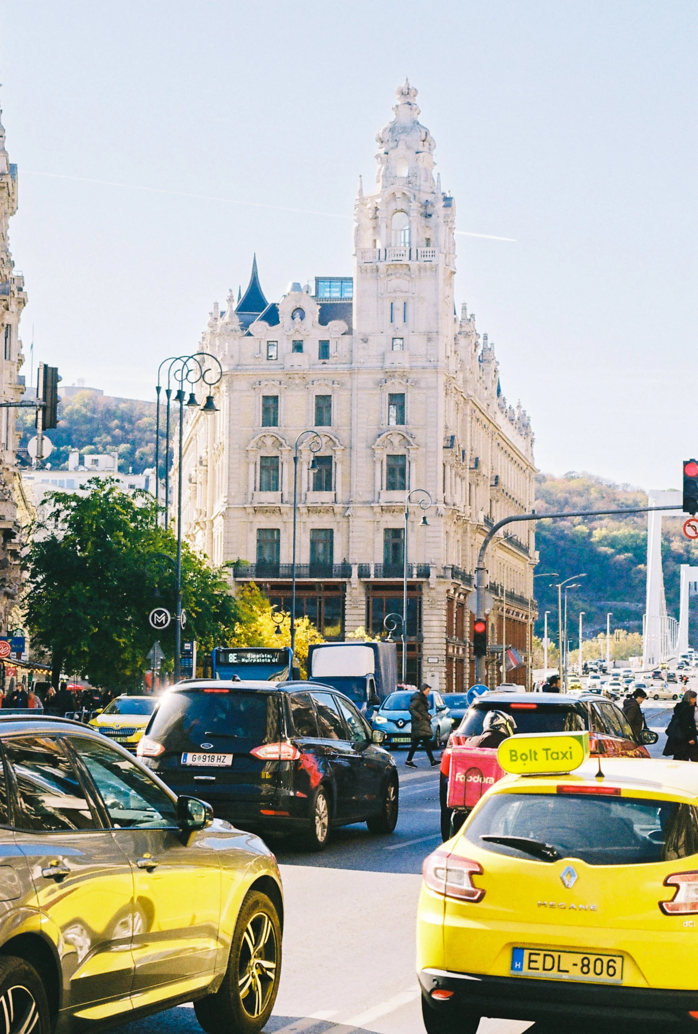 Street view in a city with traffic, a yellow taxi, and a historic building in the background.