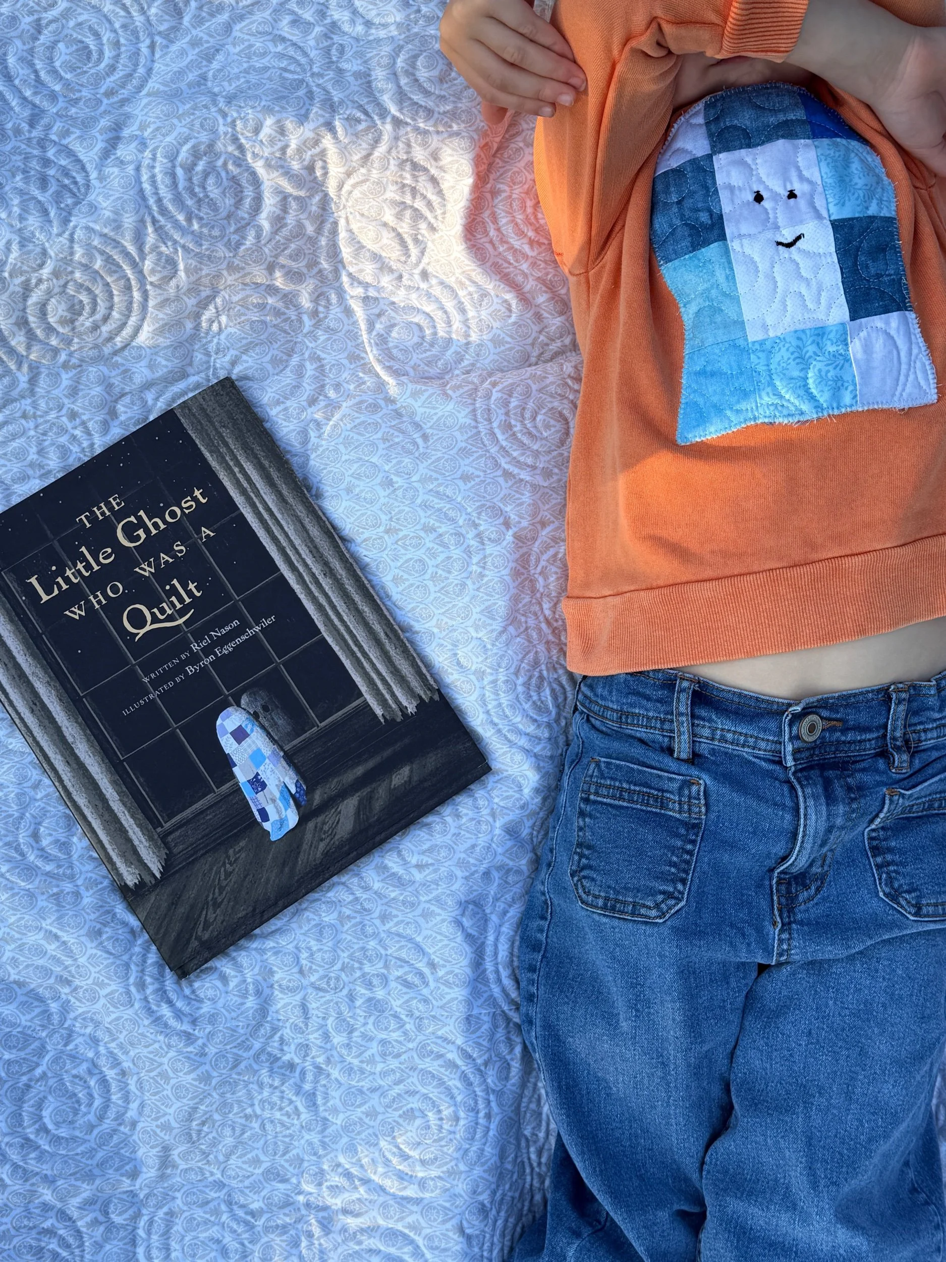 Little Ghost Who Was a Quilt picture book on comfortable quilt with child and hot sweatshirt laying down next to the book
