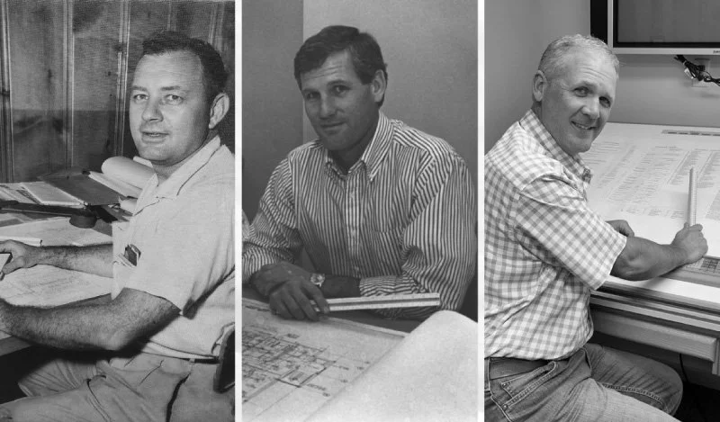 Three men sitting at desks, working with documents and blueprints, in an office or technical environment.