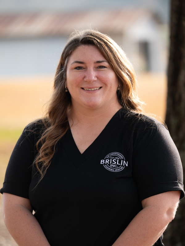 A woman smiling outdoors wearing a black shirt with a logo that says 'Brislin Inc.'