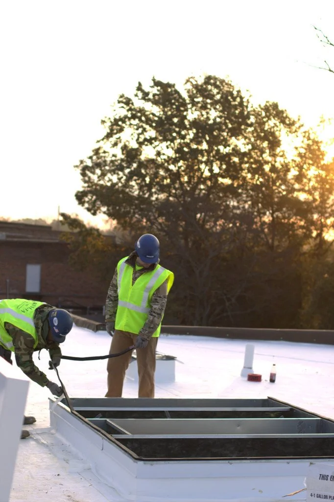 City street view during sunset with traffic lights, parked cars, buildings, and a telecommunications tower in the background.