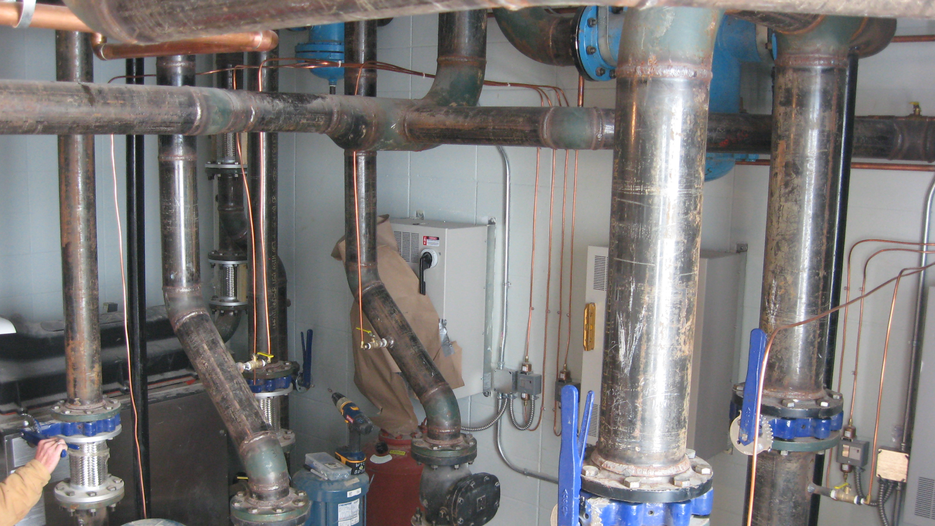 Interior view of a mechanical or boiler room with large pipes, valves, and control panels.