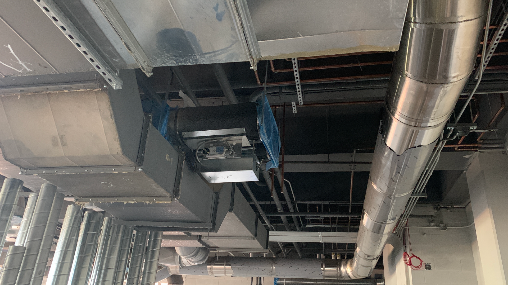 Ceiling with ductwork, pipes, and ventilation system in an unfinished building interior.