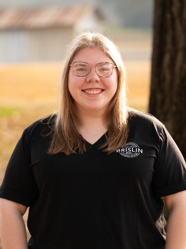 Smiling woman with glasses outdoors, wearing a black T-shirt with a logo that reads 'BRISLIN INC.'