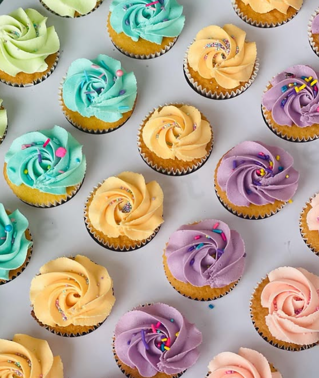 Assorted cupcakes with colorful swirled frosting and sprinkles on a white surface.