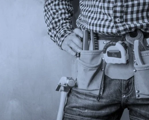 Person wearing a checkered shirt with a tool belt containing various tools and a tape measure.