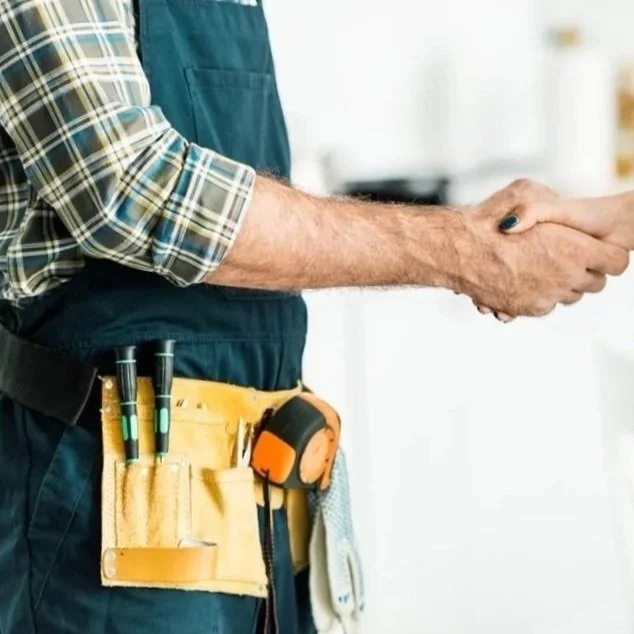 Close-up of a handyman wearing a tool belt with screwdrivers and a measuring tape, holding a phone.