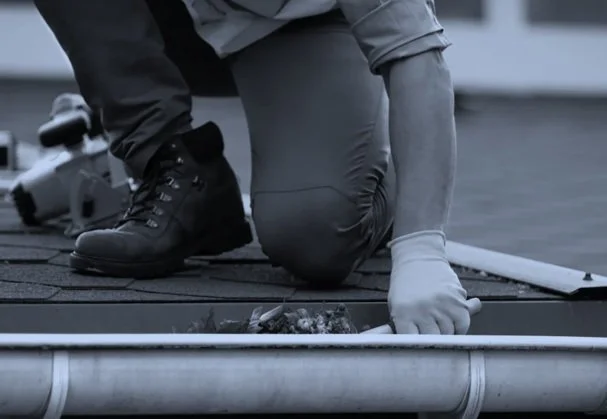 Person kneeling on a rooftop, working with plumbing while wearing work boots and gloves.