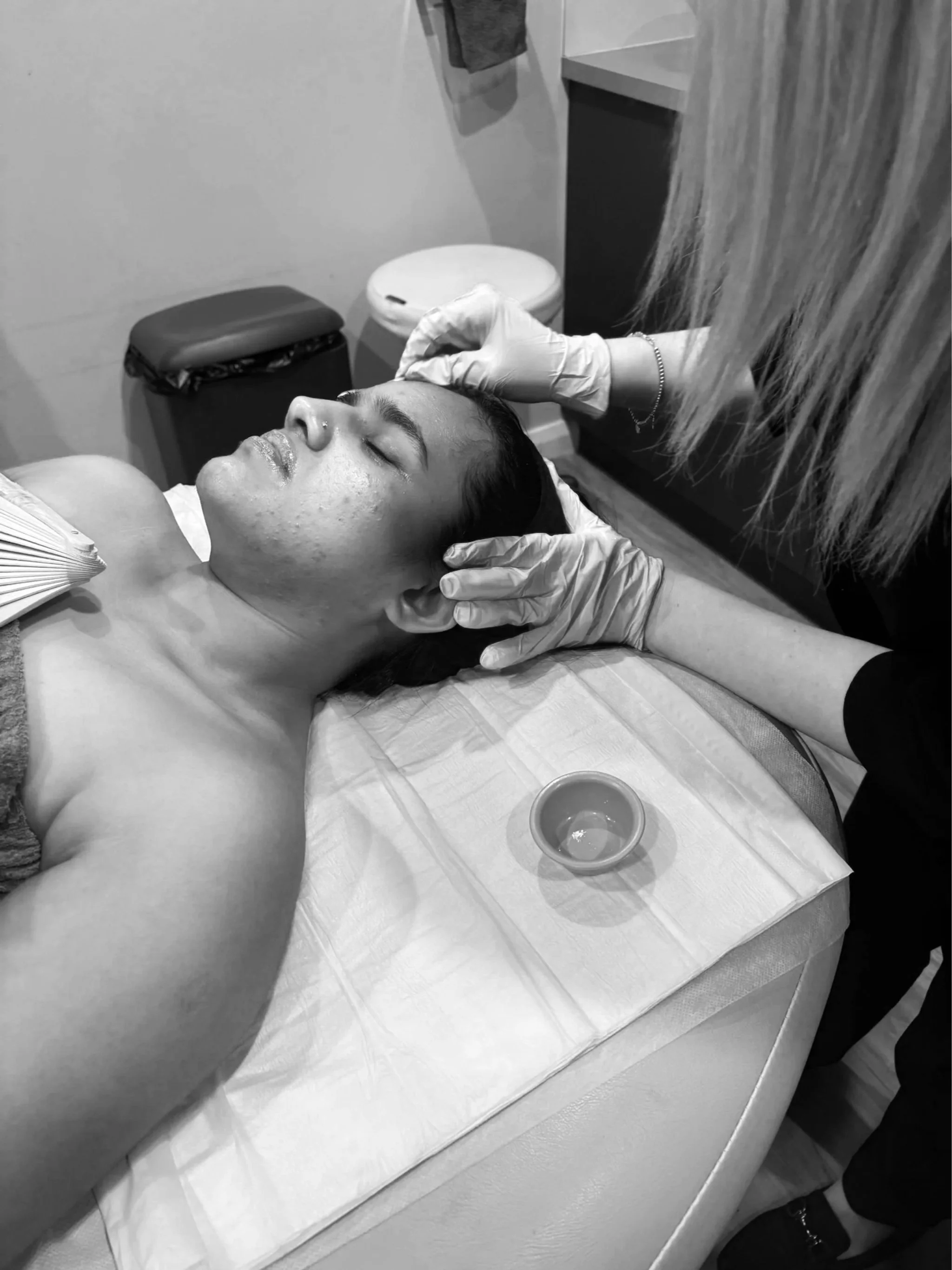 A woman receiving a facial treatment from a professional wearing gloves in a spa or clinic setting.