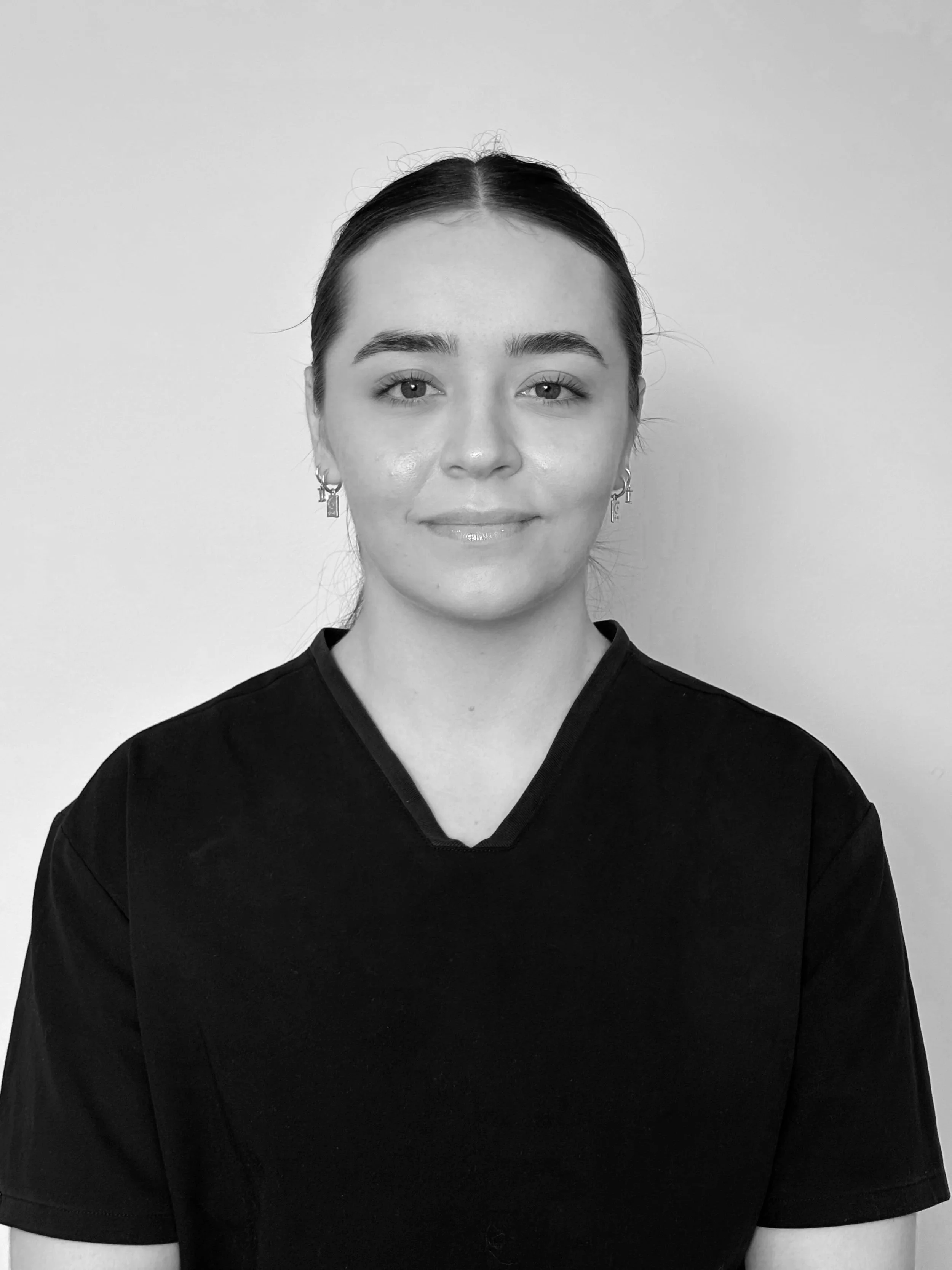 Black and white portrait of a young woman with hair pulled back, wearing earrings and a dark T-shirt, smiling softly at the camera.