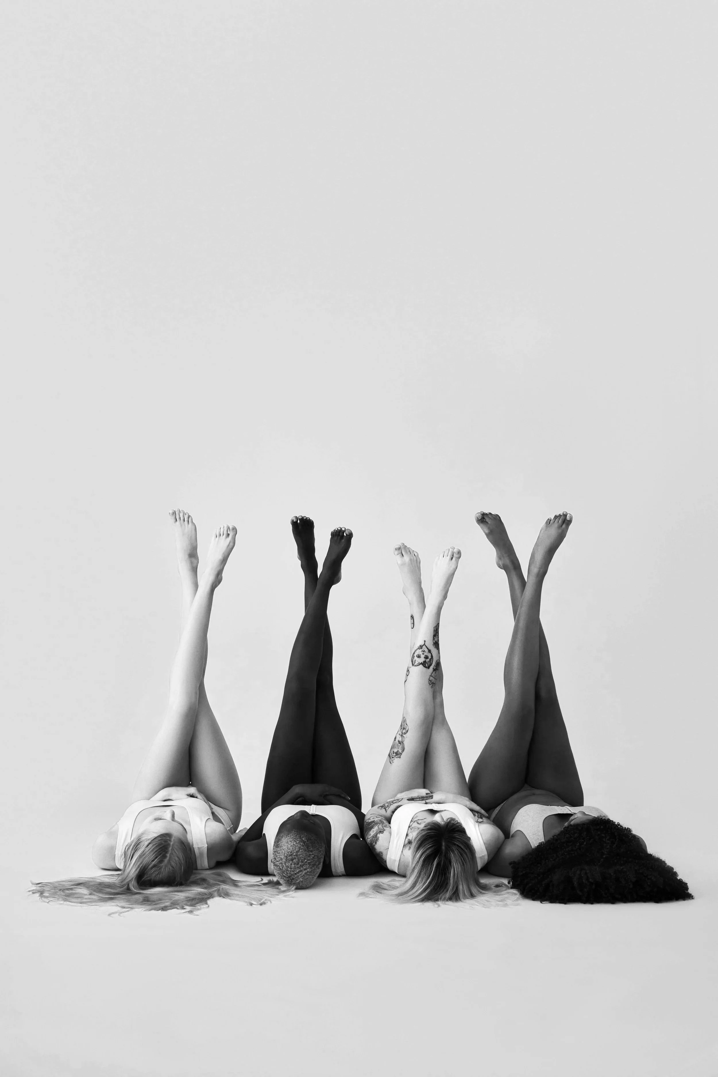Four women lying on their backs with legs raised, against a plain background.