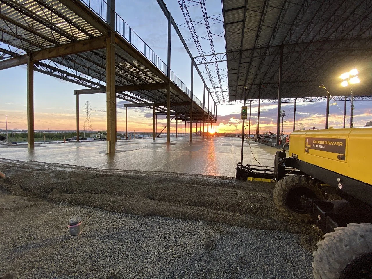 Construction site during sunset with partially built structure, construction equipment, and a clear sky with clouds.